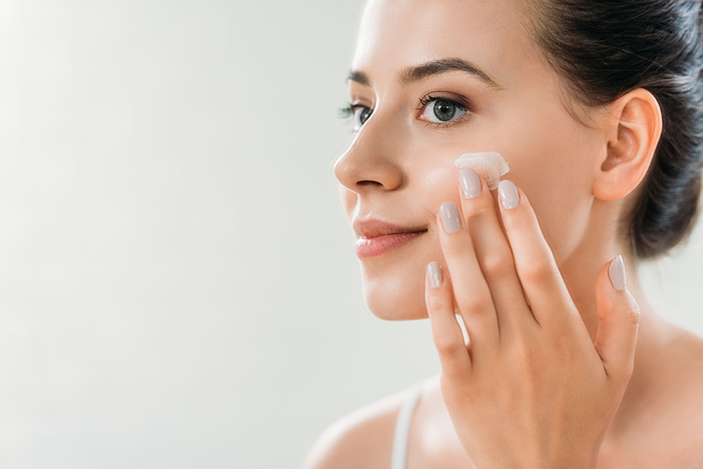 beautiful smiling young woman applying face cream and looking away